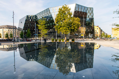 Blick auf die moderne Unibibliothek in Freiburg. Davor stehen Bäume. 